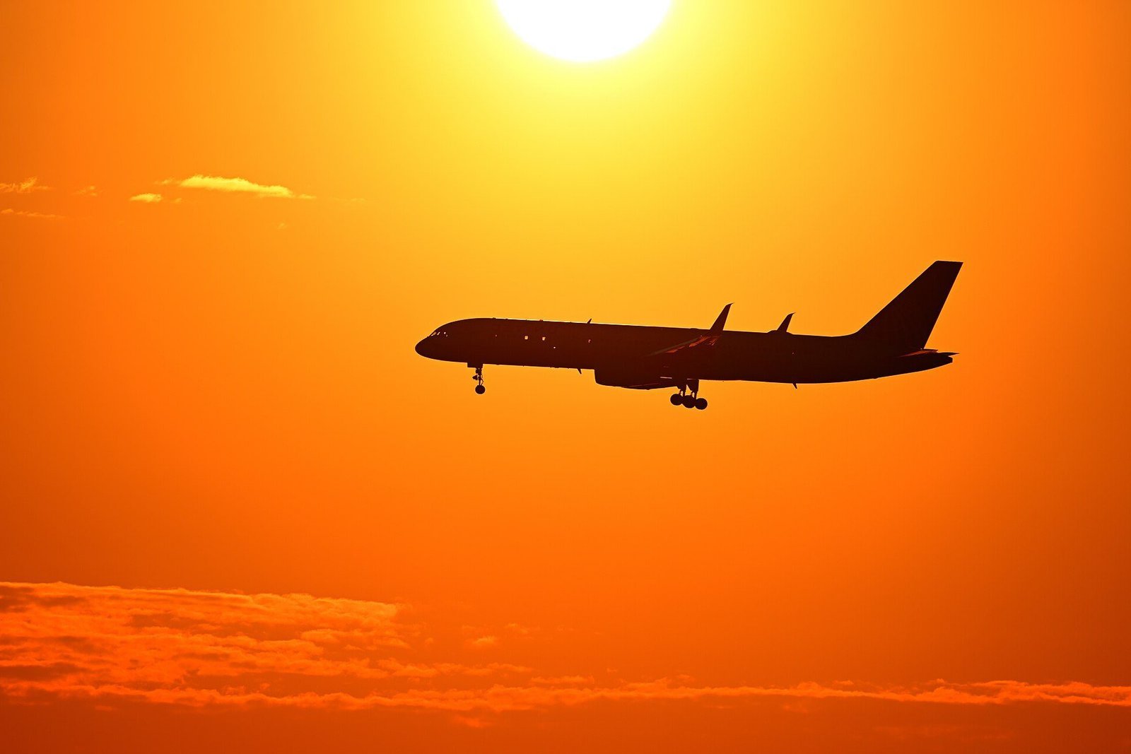 Silhouette of a Boeing 757 airliner on final approach against a glowing orange sunset sky