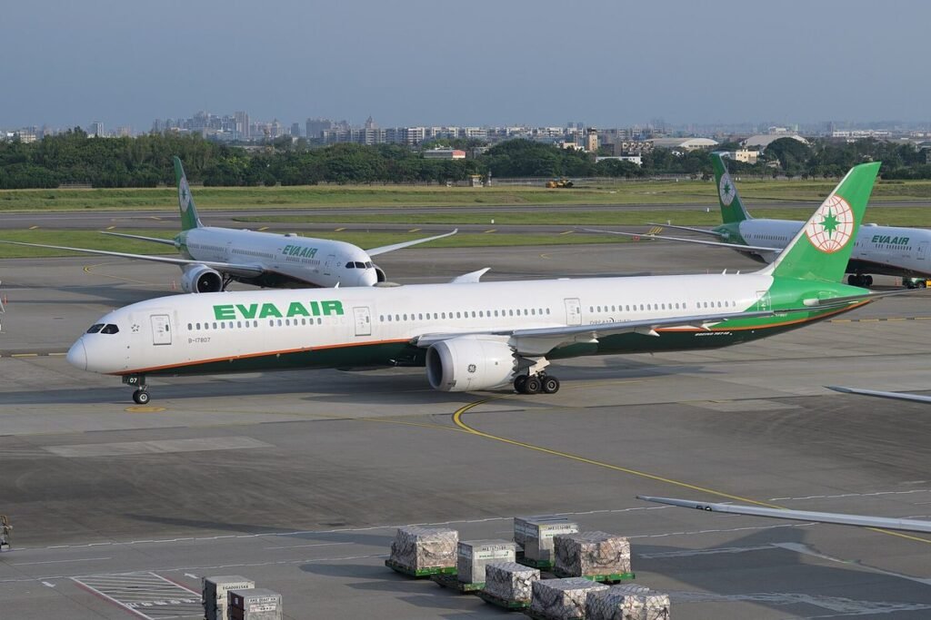 EVA Air Boeing 787-10 Dreamliner in green and white livery taxiing past cargo containers at Taoyuan International Airport