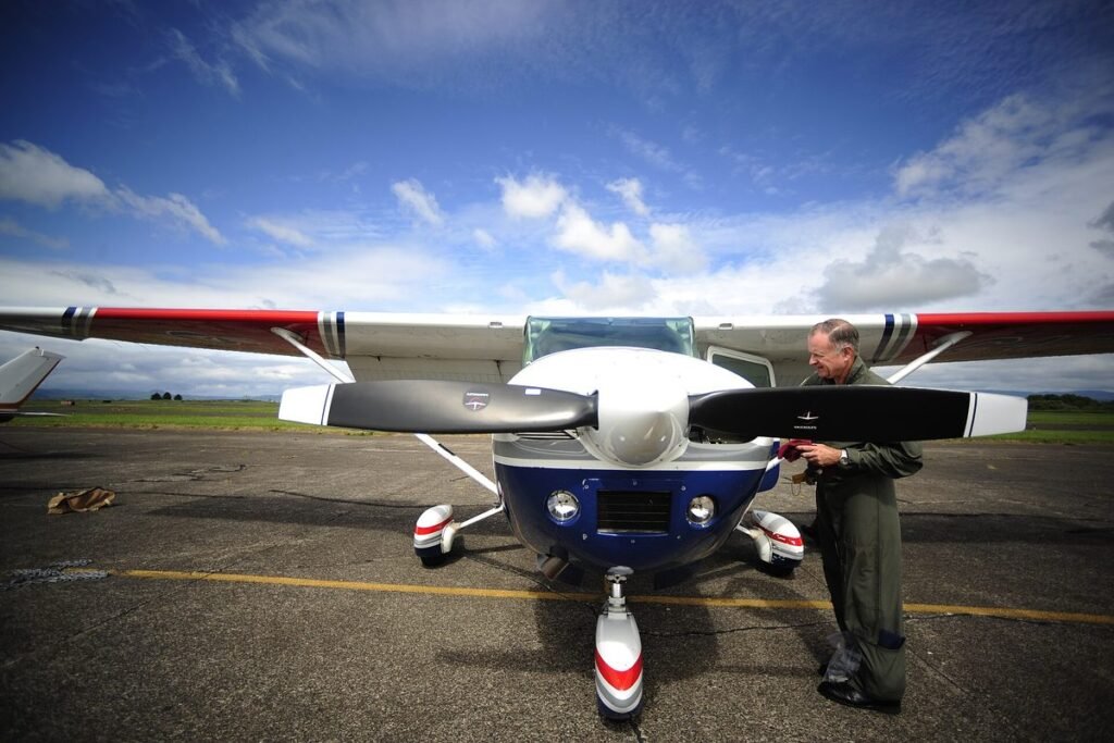 Pilot checking the engine oil of a Cessna during a preflight inspection on the ramp under a blue sky