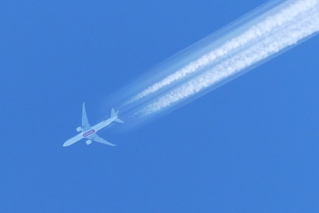 Twin-engine airliner at cruise altitude leaving white contrails across a deep blue sky