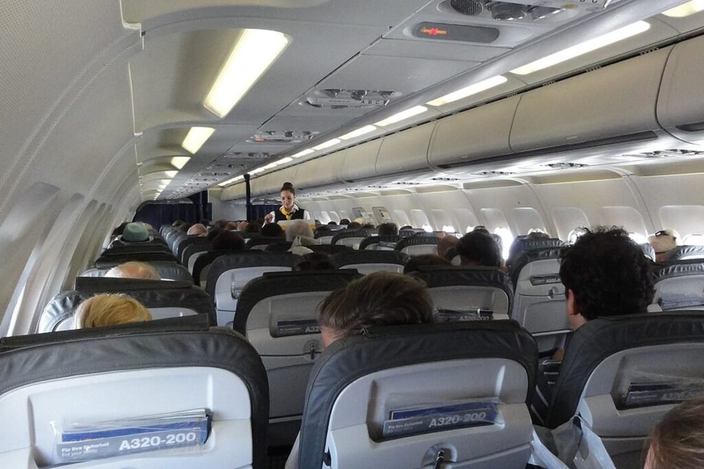 Flight attendant pouring drinks for passengers in the aisle of an Airbus A320 cabin, seen from a rear seat