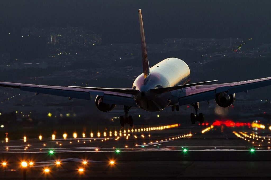 Airliner touching down at night over rows of runway approach lights with city lights in the distance