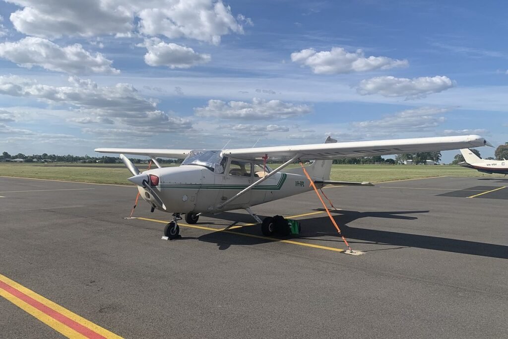 Cessna 172 tied down on an airport ramp under a bright blue sky with scattered clouds