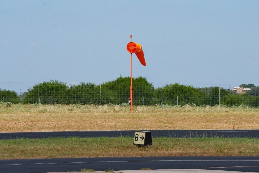 Orange windsock on a pole beside a taxiway sign at a small US airport under a clear sky