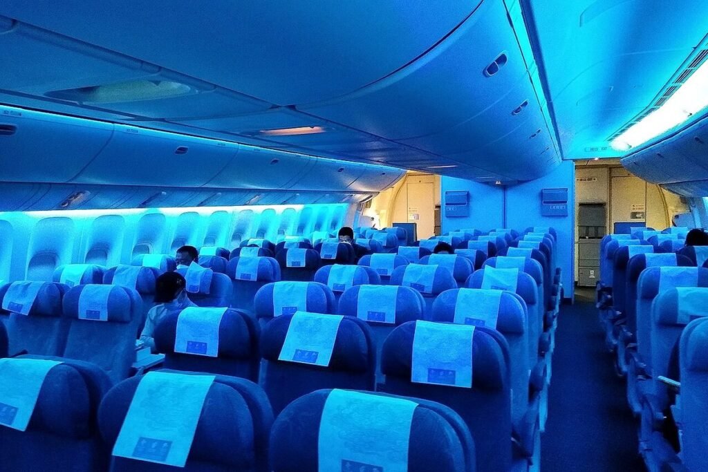 Rows of mostly empty economy class seats under blue mood lighting in a wide-body airliner cabin