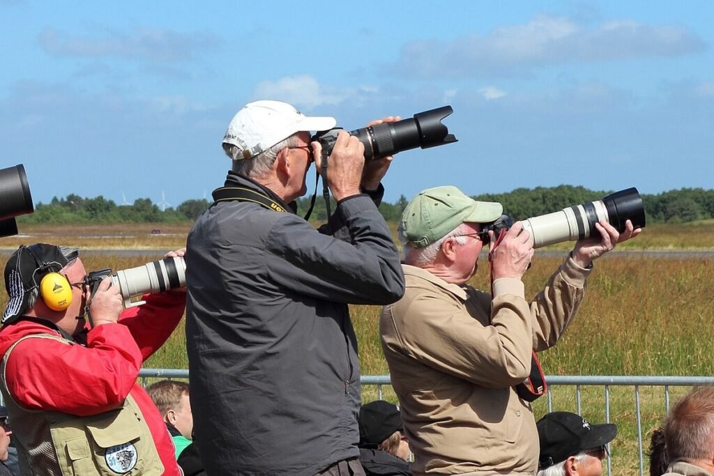 Aircraft spotters aiming DSLR cameras with long white and black telephoto lenses toward the sky at an airshow